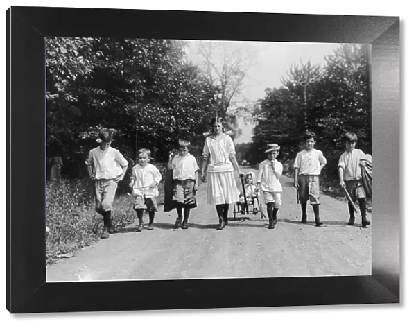 Country Walk; group of seven children walking in a row, and an eighth being pulled in a cart