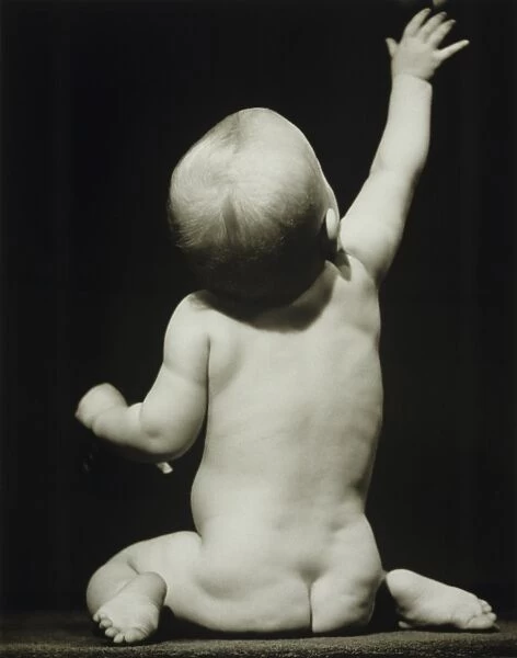 Baby boy (6-12 months) raising hand sitting in studio, (B&W)