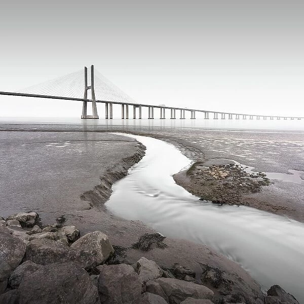 Long exposure of the famous bridge Ponte Vasco da Gama at low tide on the river Tejo with a small water tributary in Lisbon, Portugal