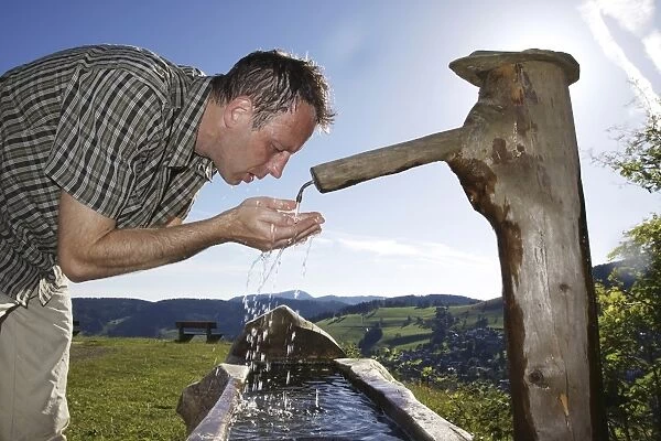 A man in his mid 40s cools off at a well, Todtnauberg in the Black Forest, Baden-Wuerttemberg, Germany, Europe