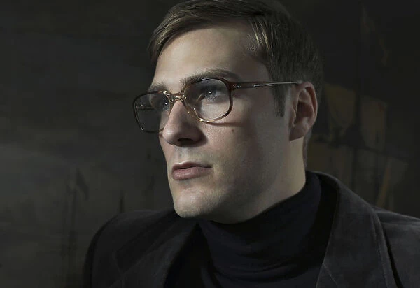 Student wearing a suit and glasses, sitting in front of a painting