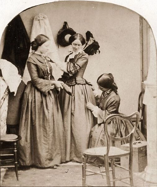Tailoring. 1860: A woman kneeling to mend anothers skirt