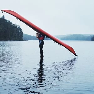 Man with kayak on head on lake surface, side view