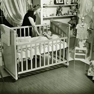 Mother looking at baby (3-6 months) lying in crib, (B&W)