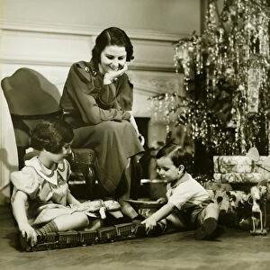 Mother watching three children playing by Christmas tree, (B&W)
