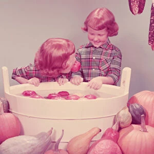 Twin red haired girls bobbing for apples at party. (Photo by H