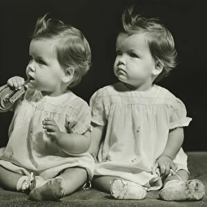 Twin sisters (9-12 months)sitting on blanket, (B&W), portrait