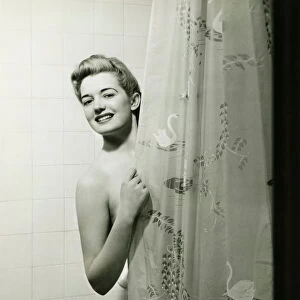 Woman standing in bathtub, peering through shower curtain, (B&W), portrait