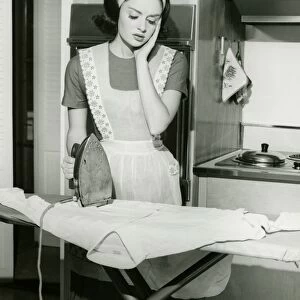 Young woman ironing in kitchen, (B&W)
