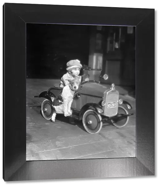 Girl in toy pedal car with dog sitting on running board