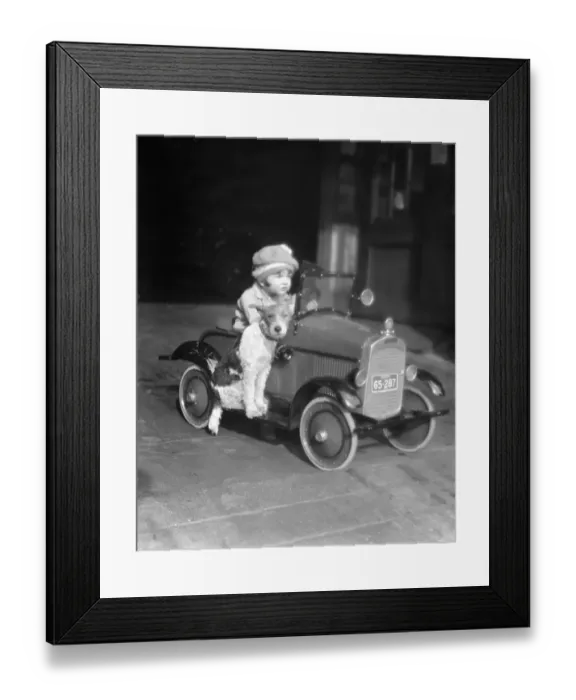 Framed Print : Girl in toy pedal car with dog sitting on running board Framed Print : Girl in toy pedal car with dog sitting on running board