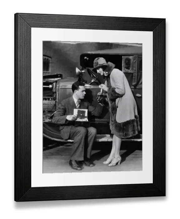 Framed Print : Woman bandaging finger of man with greasy hands, sitting on running board of car with hood open Framed Print : Woman bandaging finger of man with greasy hands, sitting on running board of car with hood open