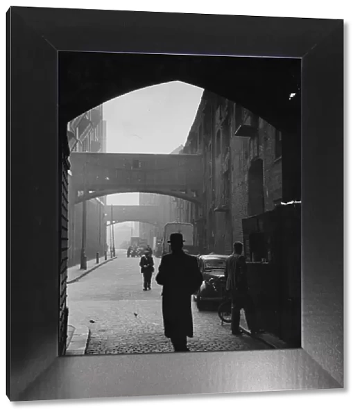 A man in a bowler hat walking under the arches on the cobbled Wapping High Street, London