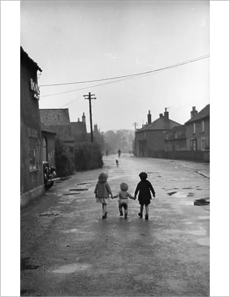 Its A Lonely Road; Three children walk hand in hand down the main street of the village