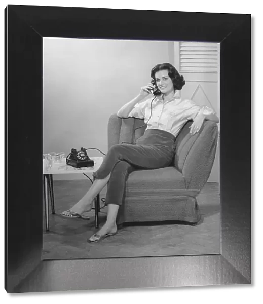 Woman sitting on armchair, talking on phone, (B&W)