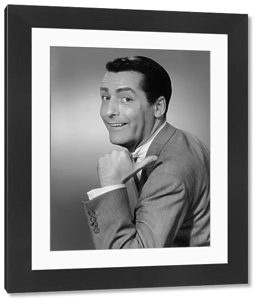 Smiling man pointing in studio, (B&W), portrait