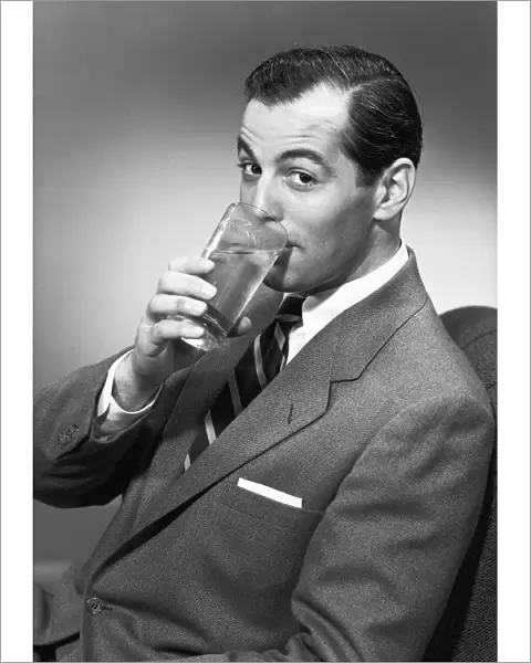 Man drinking water from glass, posing in studio, (B&W), portrait