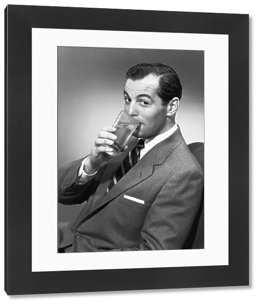 Man drinking water from glass, posing in studio, (B&W), portrait