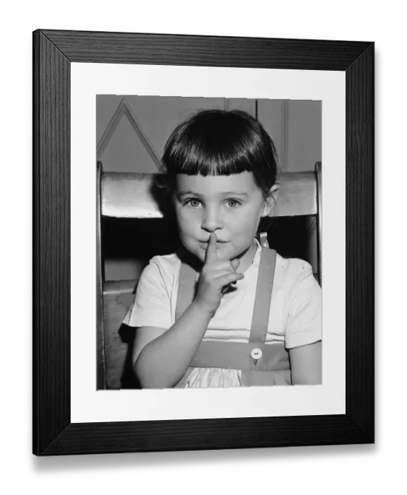 Framed Print : Girl (4-5) holding finer on mouth, (B&W), portrait