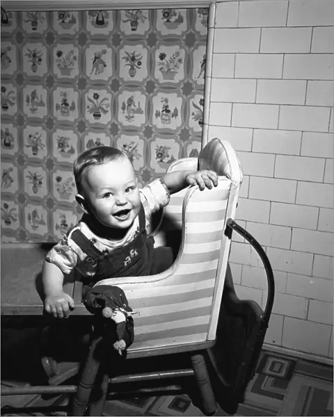 Boy (2-3) sitting in high chair, (B&W), portrait