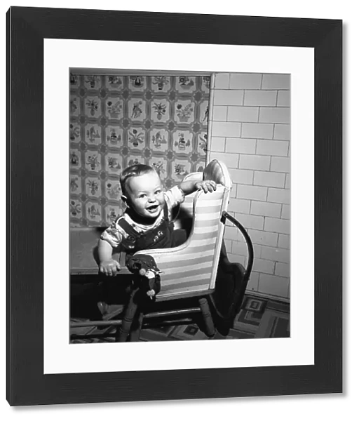 Boy (2-3) sitting in high chair, (B&W), portrait