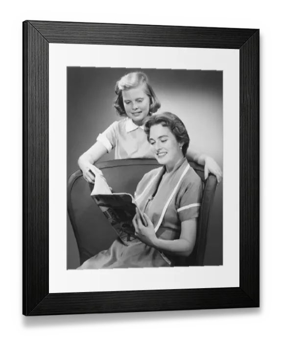 Framed Print : Girl (8-9) standing at mother reading magazine, (B&W) Framed Print : Girl (8-9) standing at mother reading magazine, (B&W)