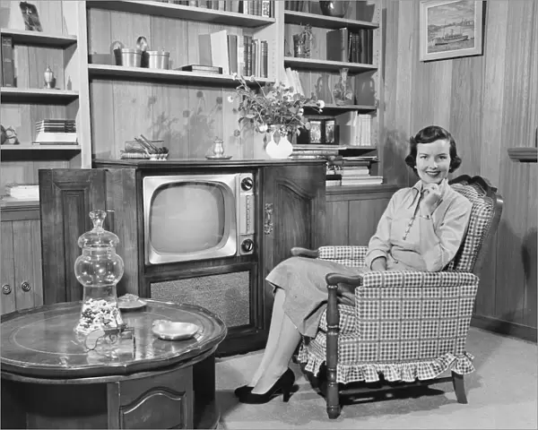 Woman sitting in armchair in living room, (B&W), portrait