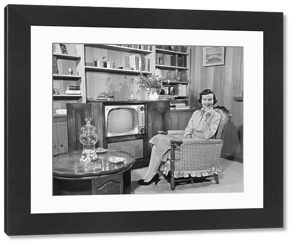 Woman sitting in armchair in living room, (B&W), portrait