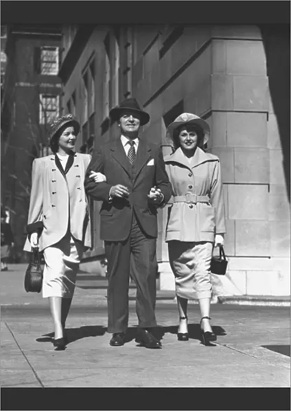 Man and two women walking on sidewalk, (B&W)