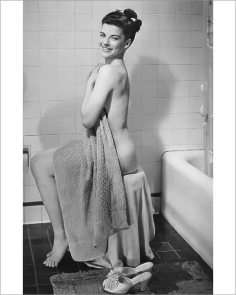 Woman sitting in bathroom, covering herself with towel, (B&W), portrait