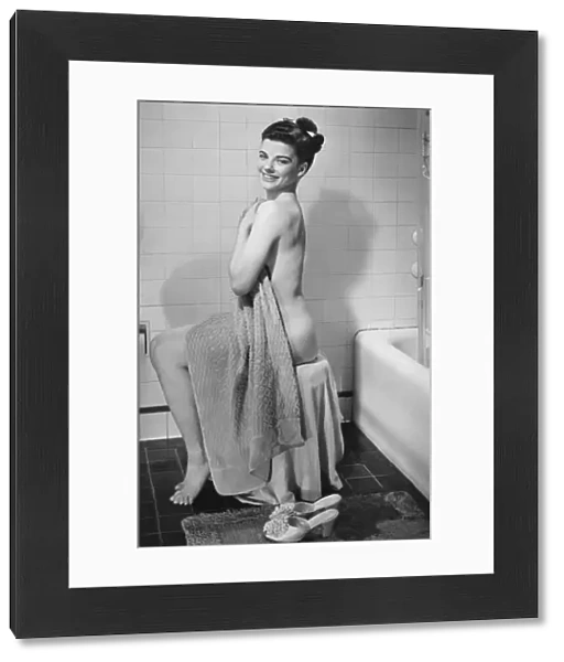 Woman sitting in bathroom, covering herself with towel, (B&W), portrait