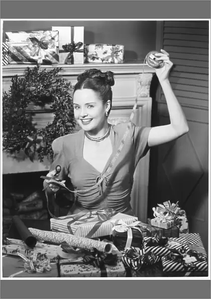 Woman wrapping Christmas presents in living room, (B&W), portrait