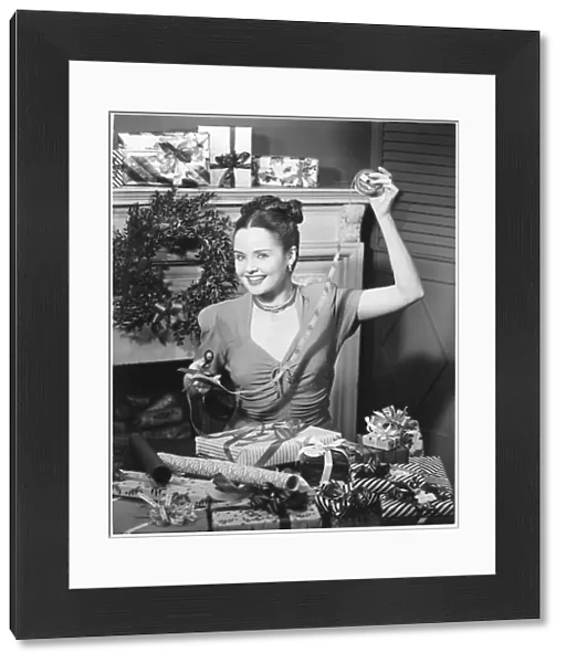 Woman wrapping Christmas presents in living room, (B&W), portrait