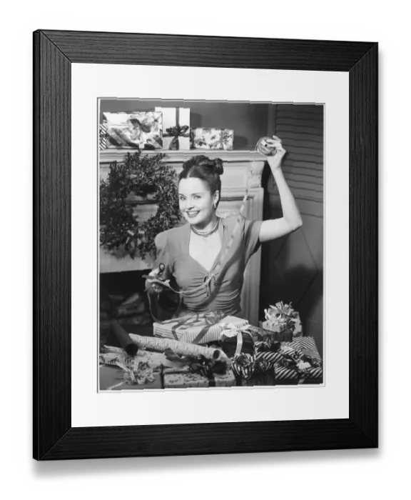 Framed Print : Woman wrapping Christmas presents in living room, (B&W), portrait Framed Print : Woman wrapping Christmas presents in living room, (B&W), portrait