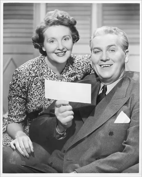 Mature couple posing, man holding check, (B&W), portrait