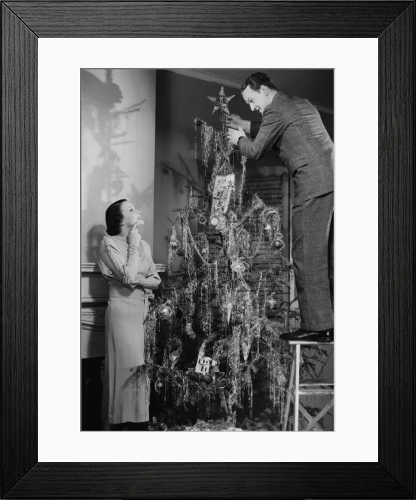 Framed Print : Woman assisting man placing star on top of Christmas tree, (B&W)