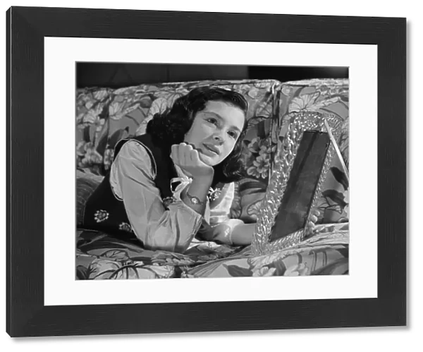 Girl (8-9) lying on couch, holding framed photo, (B&W)