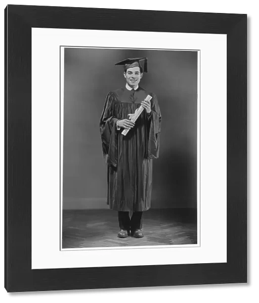 Man in graduation gown posing in studio, (B&W), portrait
