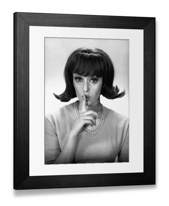 Framed Print : Woman making silence gesture in studio, (B&W), portrait Framed Print : Woman making silence gesture in studio, (B&W), portrait