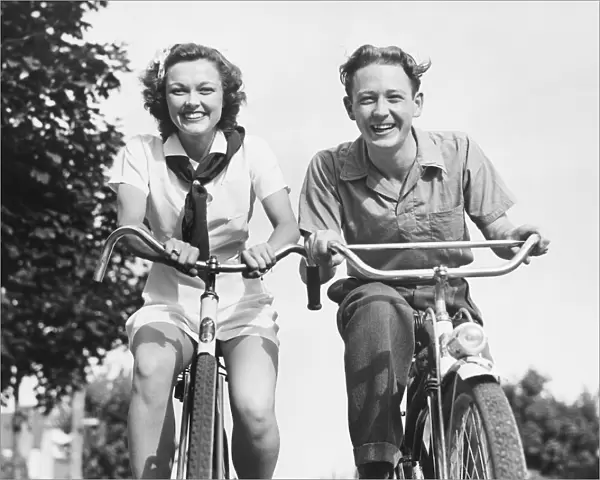 Man and woman riding bikes, (B&W), low angle view