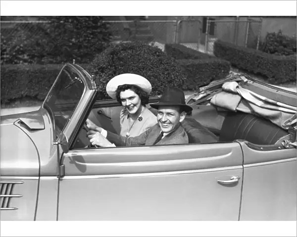Couple riding in old fashion convertible car, (B&W), , portrait