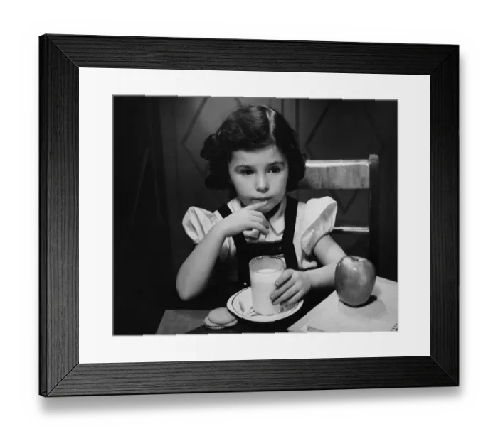 Framed Print : Girl (6-7) sitting at table, having breakfast, (B&W) Framed Print : Girl (6-7) sitting at table, having breakfast, (B&W)