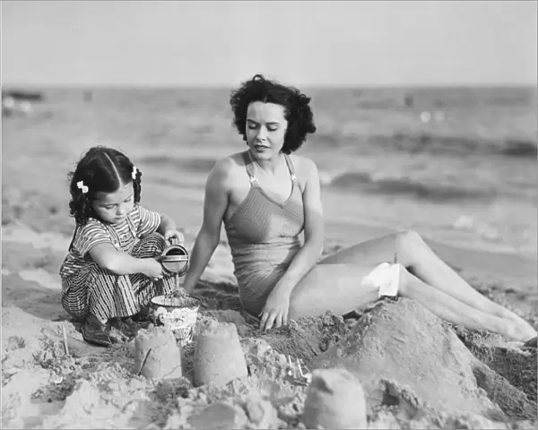 Mother with girl (2-3) playing in sand on beach, (B&W)
