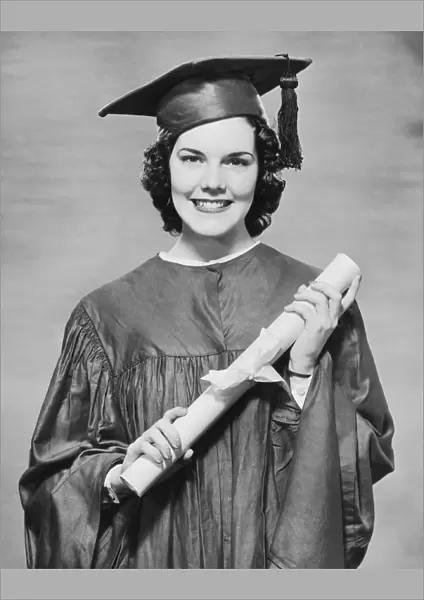 Woman wearing graduation gown holding diploma, (B&W), portrait