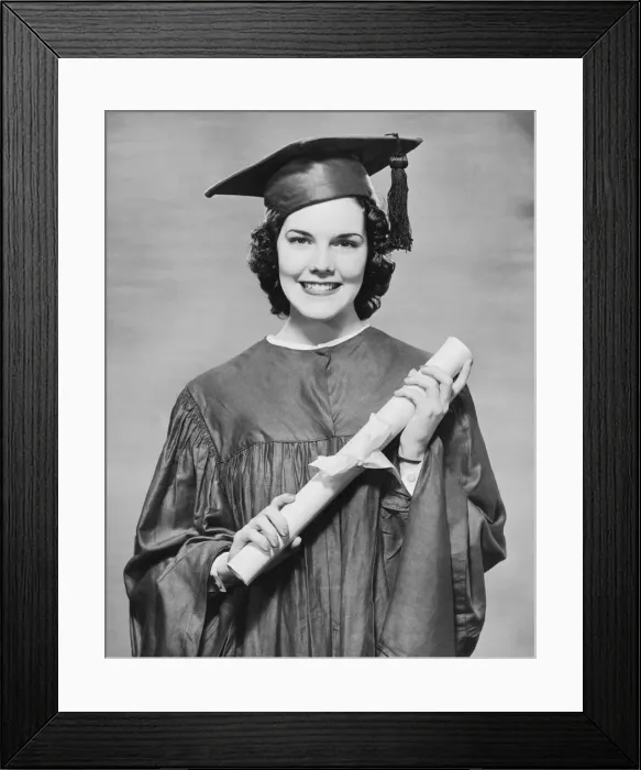 Framed Print : Woman wearing graduation gown holding diploma, (B&W), portrait Framed Print : Woman wearing graduation gown holding diploma, (B&W), portrait