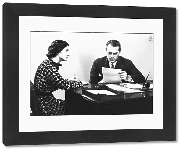 Secretary assisting businessman reading document at desk, (B&W)