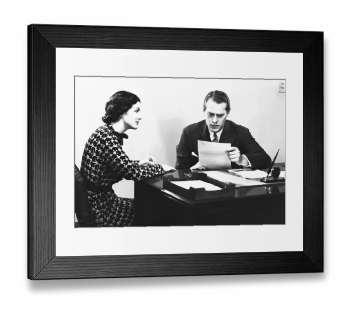 Framed Print : Secretary assisting businessman reading document at desk, (B&W) Framed Print : Secretary assisting businessman reading document at desk, (B&W)