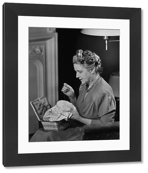 Mature woman sitting in living room, doing needlepoint, (B&W)