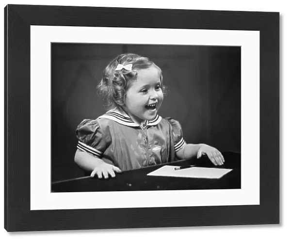 Girl (4-5) sitting at table, smiling, (B&W)