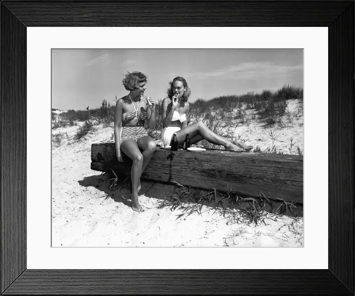 Framed Print : Two women in bikini eating snack on beach, (B&W) Framed Print : Two women in bikini eating snack on beach, (B&W)